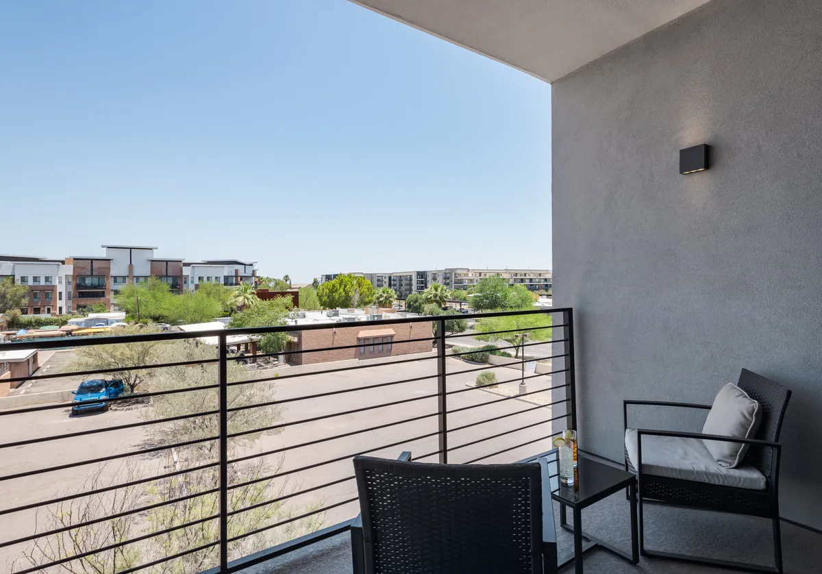 A tranquil balcony scene featuring comfortable seating, modern railing, and a city view. The space is bathed in natural light, ideal for a peaceful drink, reading, or soaking in the morning sun.