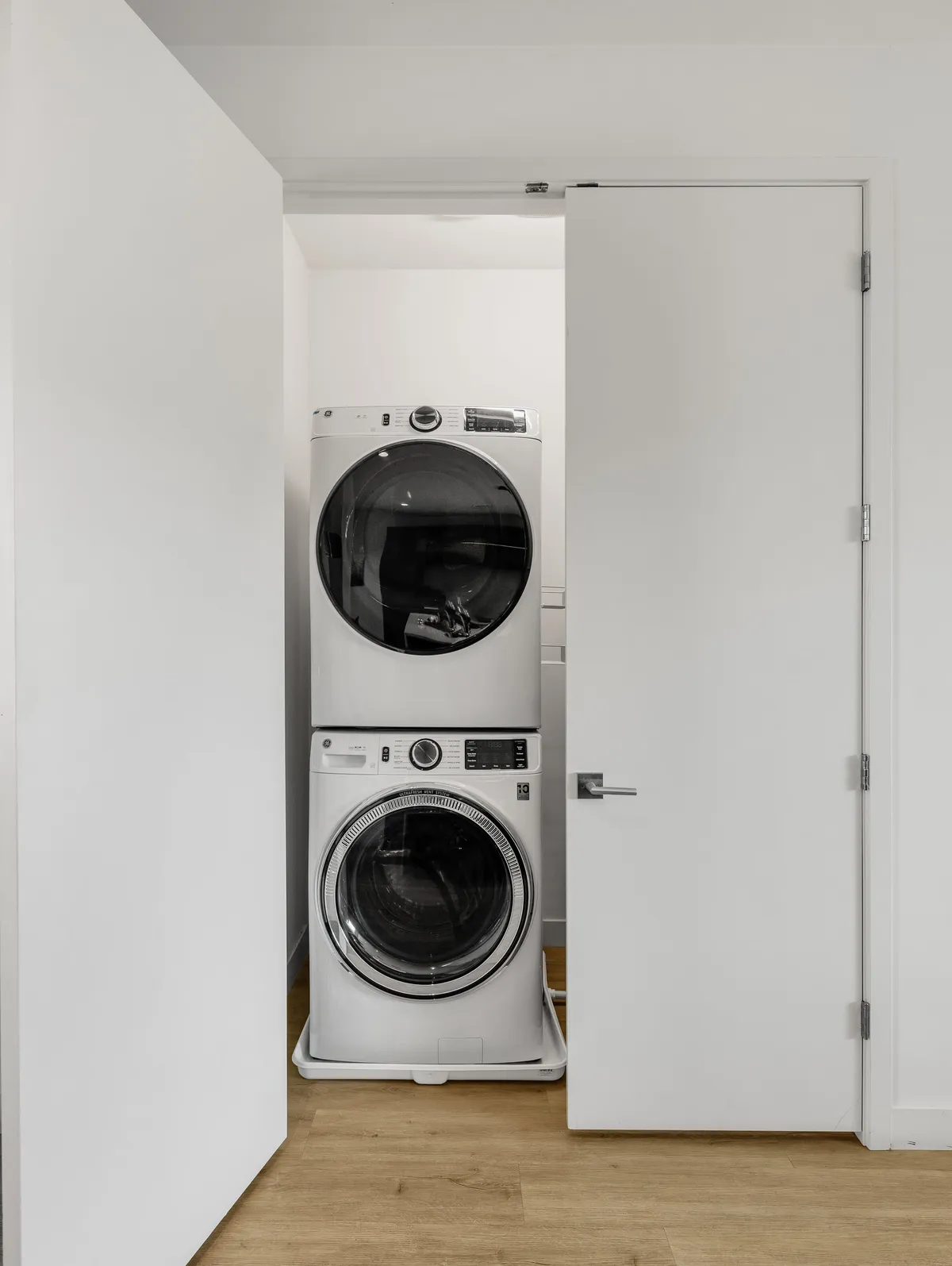 A dedicated laundry area with a stacked washer and dryer, white doors, and clean wooden floors. The space is functional, organized, and designed for practical everyday use.
