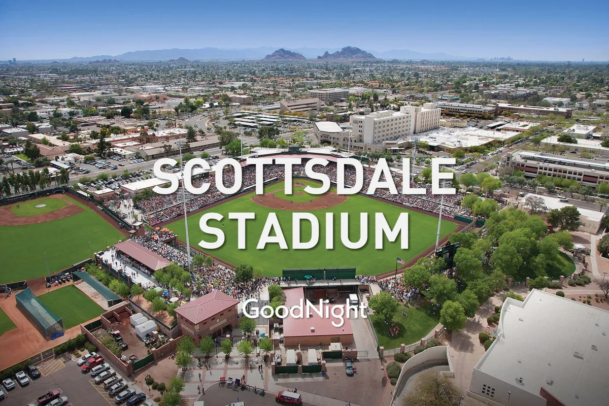 A dynamic baseball field scene at Scottsdale Stadium, with a crowd of spectators, surrounding buildings, and mountains in the background. The mood is exciting and communal, capturing the thrill and sense of community at a live game or event.