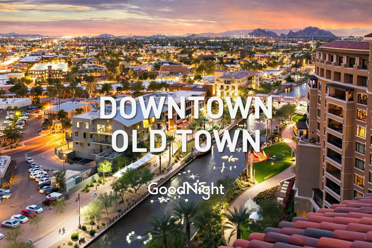 A panoramic view of Scottsdale’s illuminated cityscape at dusk, showcasing the city skyline, the tranquil canal, and distant mountains. The vibrant atmosphere hints at nightlife, dining, and upscale urban experiences along the waterfront.