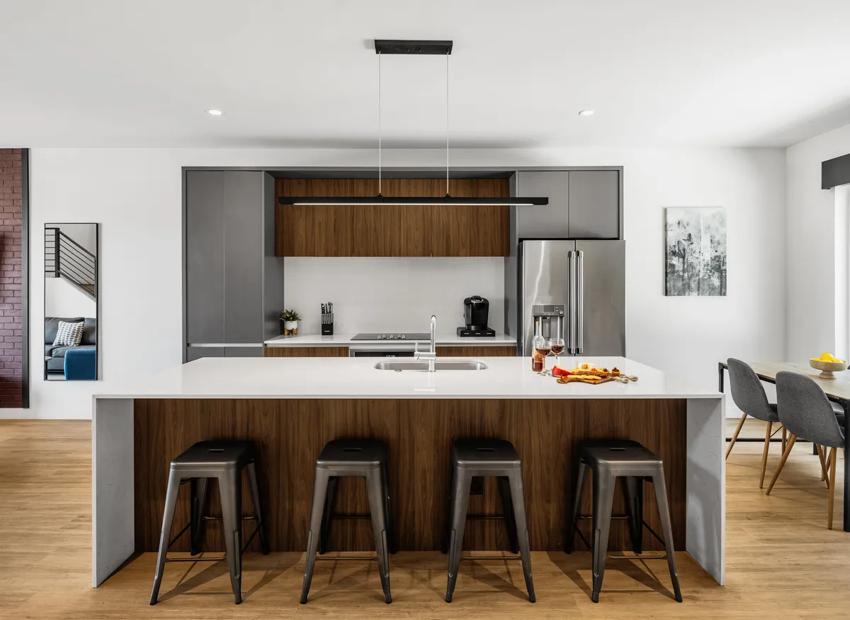 A stylish kitchen and dining area with a central island countertop, modern appliances, bar stools, and a coordinated lighting fixture. The space invites cooking, dining, and socializing, and communicates a welcoming, well-appointed environment.
