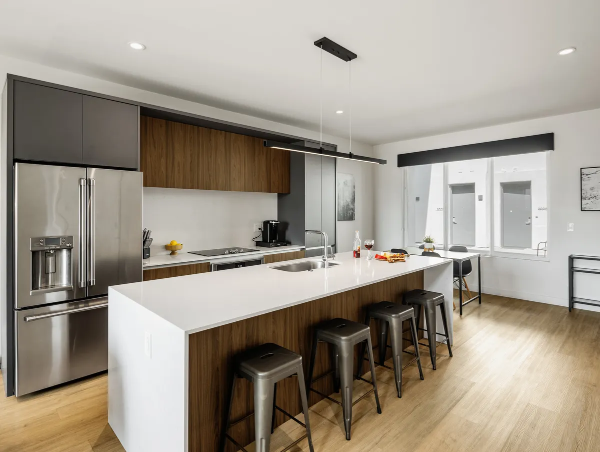 A contemporary kitchen with a central island, stainless steel appliances, bar stools, and large windows. The space is bright, welcoming, and designed for both cooking and gathering, with plenty of room to mingle.