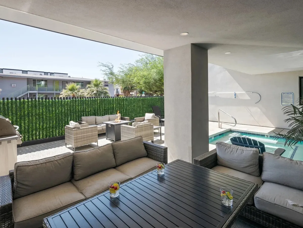 A vibrant exterior scene featuring a resort-style swimming pool surrounded by lush greenery and comfortable seating areas. Decorative drinks are placed on tables, suggesting a sociable and relaxed atmosphere perfect for unwinding or informal team gatherings. The pool area is framed by palm trees and a well-maintained patio, evoking a sense of leisure and resort-inspired comfort.