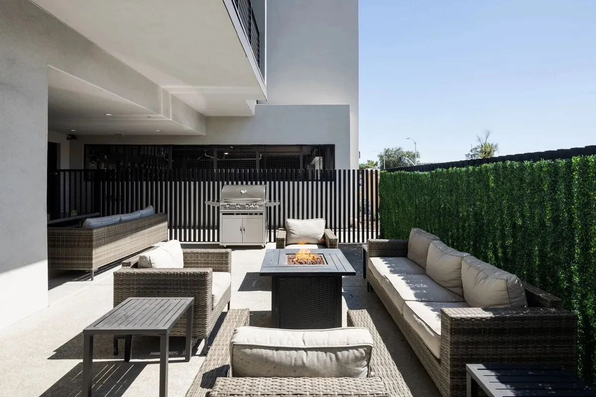 An exterior vantage of an outdoor seating area complete with a fire pit, grill, and green hedges. The scene is set for barbecuing, socializing, and enjoying outdoor meals, with a warm, communal vibe perfect for evenings and group feasts.