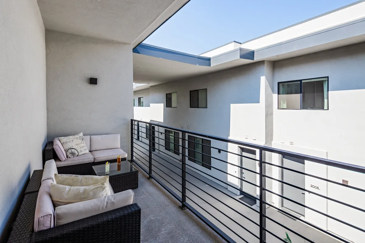 This image features a private outdoor seating area on a balcony with a clear blue sky as the backdrop. The balcony is furnished for comfort, providing a perfect spot for relaxing, enjoying a drink, or taking in the sunrise or stars at night.