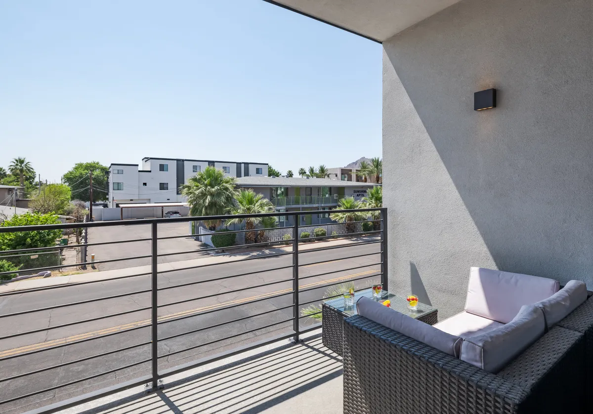 An inviting exterior balcony seating area overlooking a street lined with palm trees. The scene includes a table set with drinks, suggesting relaxation and enjoyment of the urban surroundings, perfect for people-watching or unwinding after a night out.