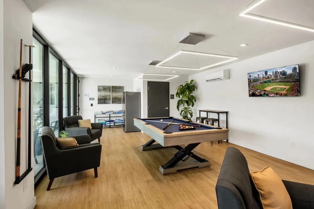 This image showcases the clubhouse interior, focusing on a pool table, a television, comfortable seating, and an indoor plant. The setting is casual and fun, encouraging group activities such as playing pool, watching sports, and socializing in a relaxed environment.