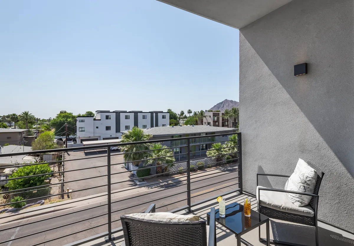 A stylish balcony with comfortable seating overlooks a mountain view and an urban landscape. The scene suggests a peaceful moment for morning coffee, small-group discussions, or winding down after a productive day, all while being immersed in Scottsdale’s vibrant surroundings.