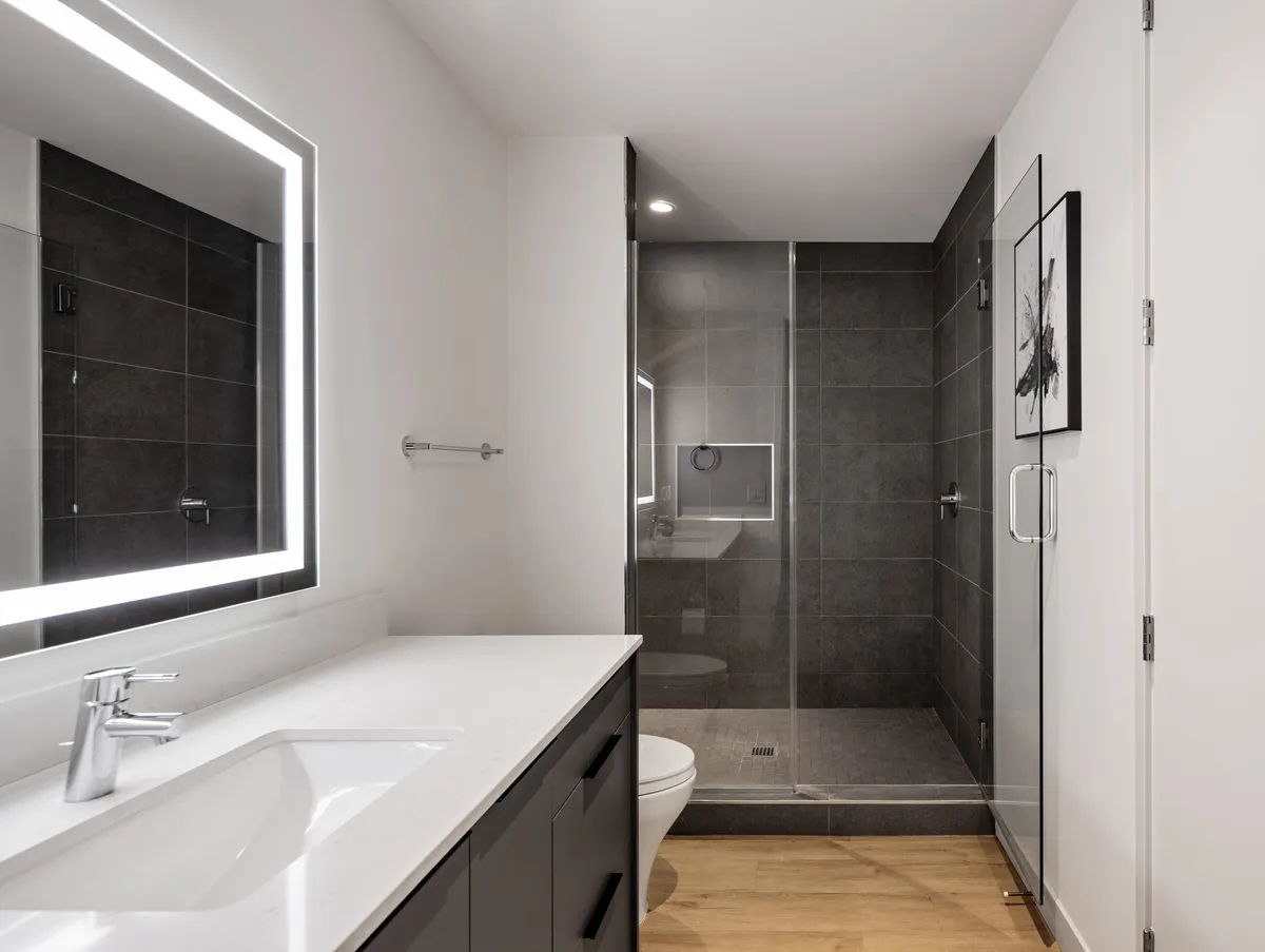 A modern en-suite bathroom with an illuminated mirror, glass shower enclosure, and sleek vanity. The setup is contemporary and spa-like, ideal for self-care routines and relaxation after a long day.